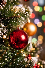 Load image into Gallery viewer, A shiny red Christmas ball ornament hanging on a decorated evergreen tree with warm string lights and blurred multicolored bokeh lights in the background.