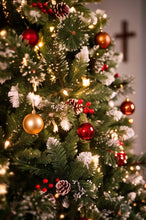 Load image into Gallery viewer, A close-up of a decorated Christmas tree with green branches, white faux snow, warm white string lights, red and gold ornaments, pinecones, and red berries. A dark wooden cross is faintly visible on the wall in the background.
