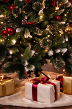 Load image into Gallery viewer, A decorated Christmas tree with red ornaments, gold and white lights, and white wrapped gifts on a cream fabric tree skirt, with one gift in the foreground tied with a dark red ribbon.
